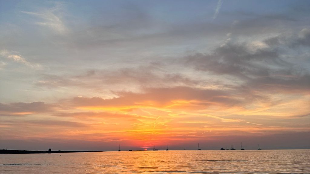 Tramonto sul mare con barche all’orizzonte