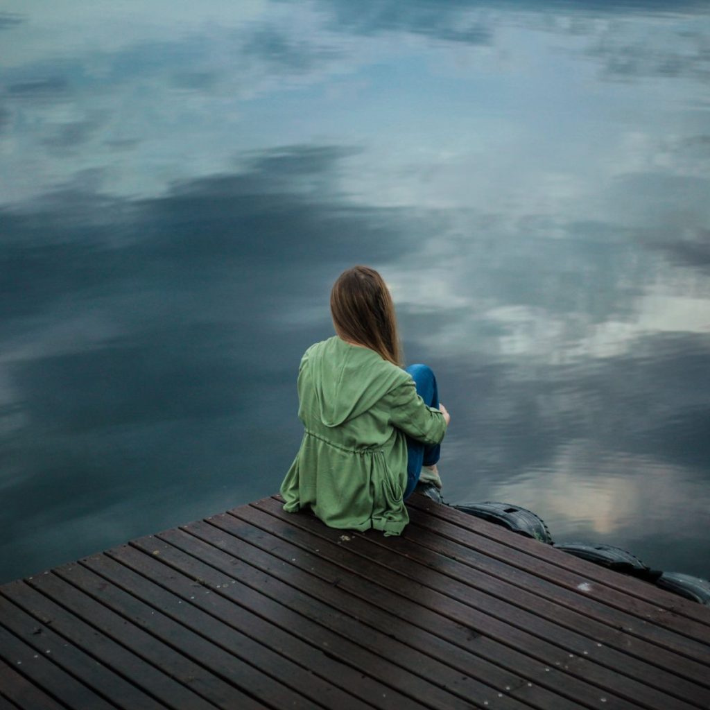 Donna di spalle seduta su un pontile di legno mentre guarda l'acqua, simbolo di introspezione e ascolto di sé in un momento di crisi lavorativa